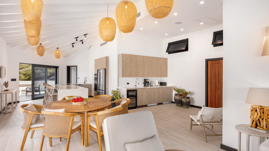 A kitchen at Tamarind Hills Resort and Villas, Antigua, with cabinets, appliances, a kitchen island with bar stools, a dining table with chairs and pendant lights hanging from the ceiling.