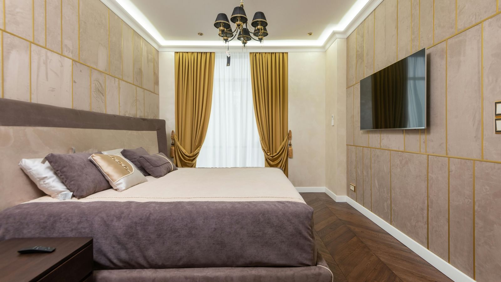 A modern bedroom showcases a large bed, wooden panelling on the walls, and indirect lighting illuminating the space.