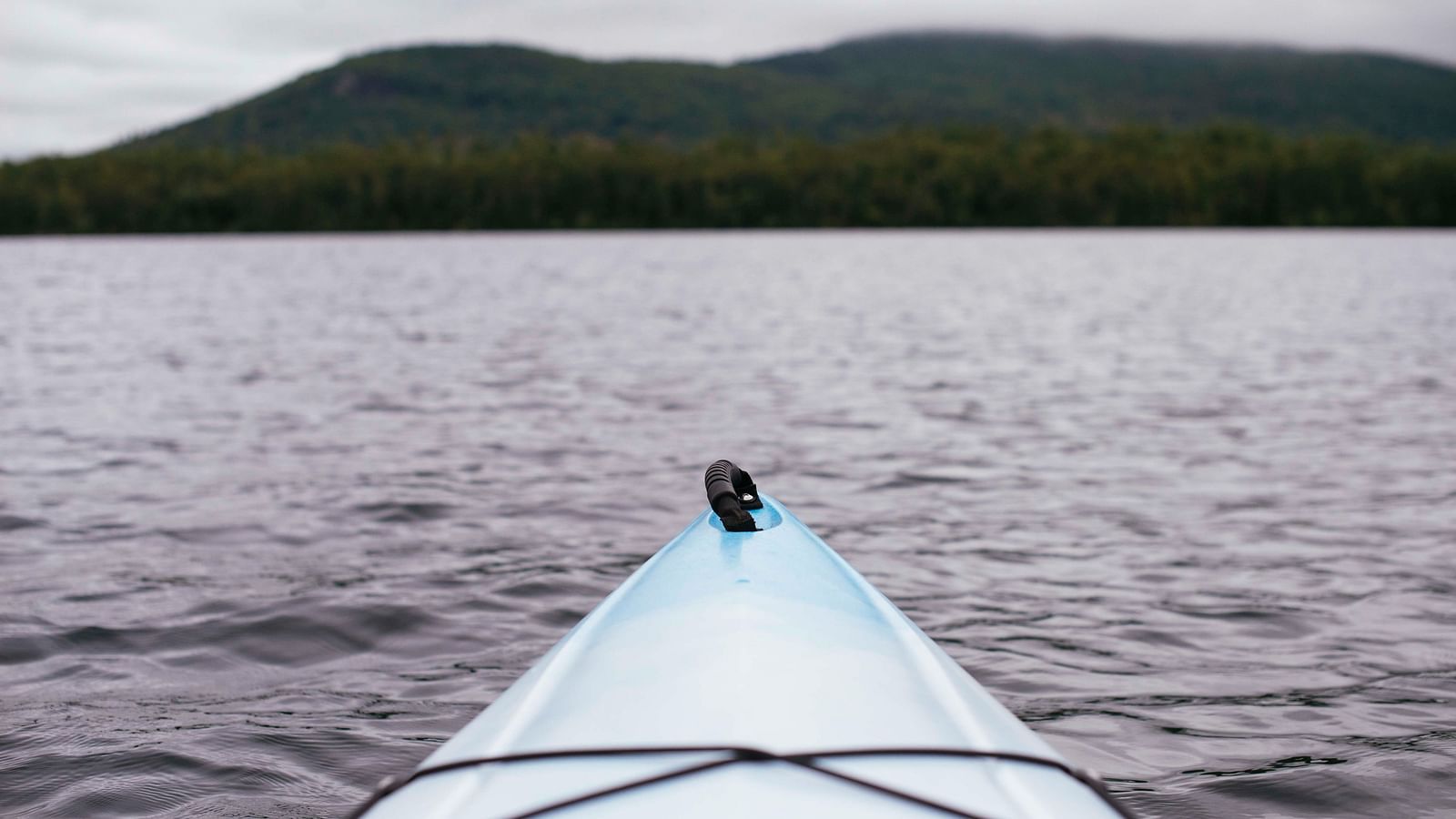 The tip of a kayak in view that is in water with an island in the background