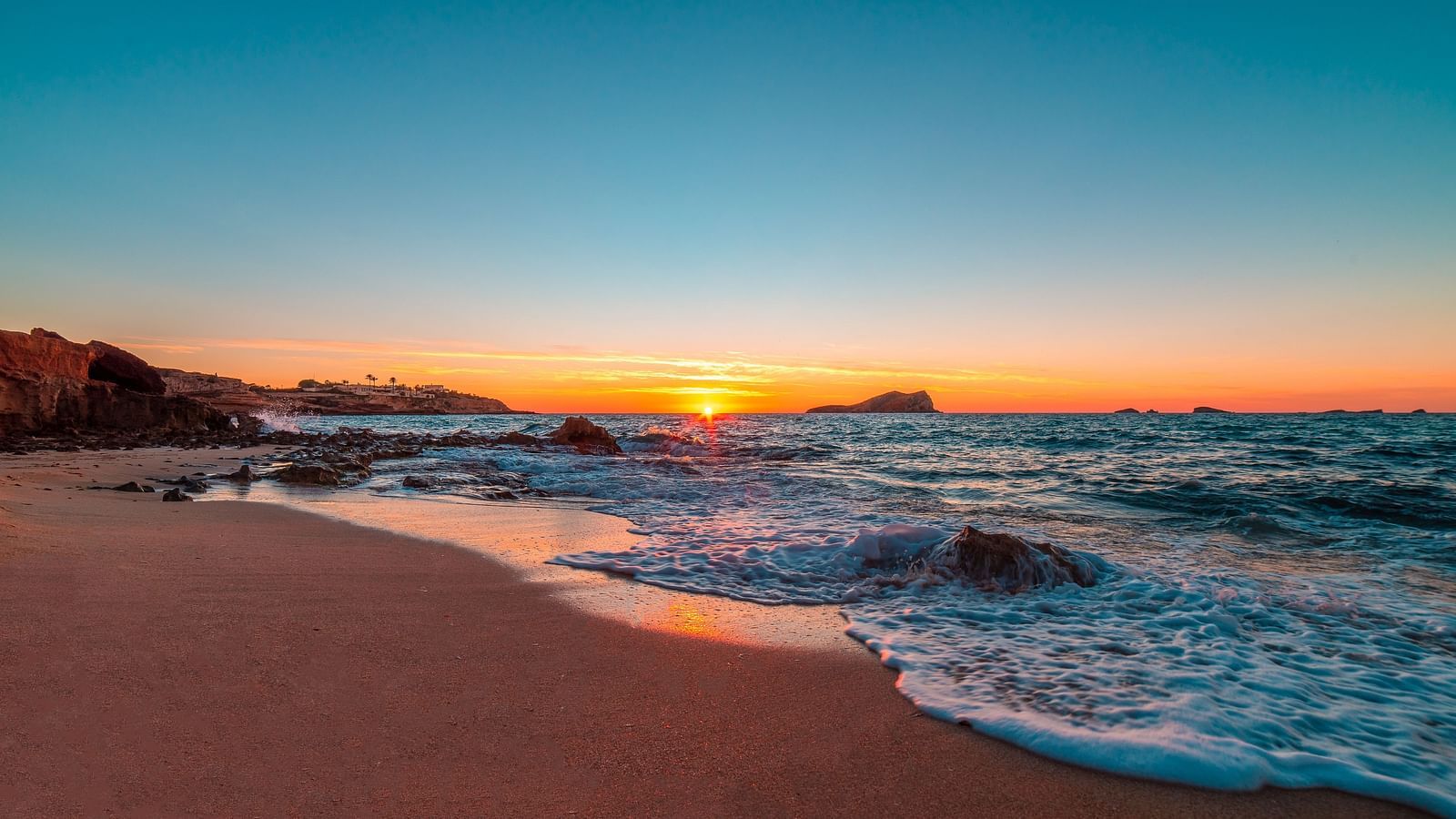 Waves meeting the shore at sunset with the sun setting in the background