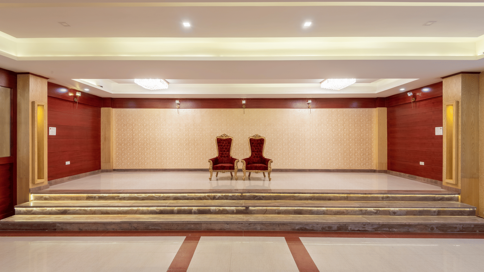 A raised stage with 2 ornate chairs positioned at the front in a banquet hall of DLS Hotels.