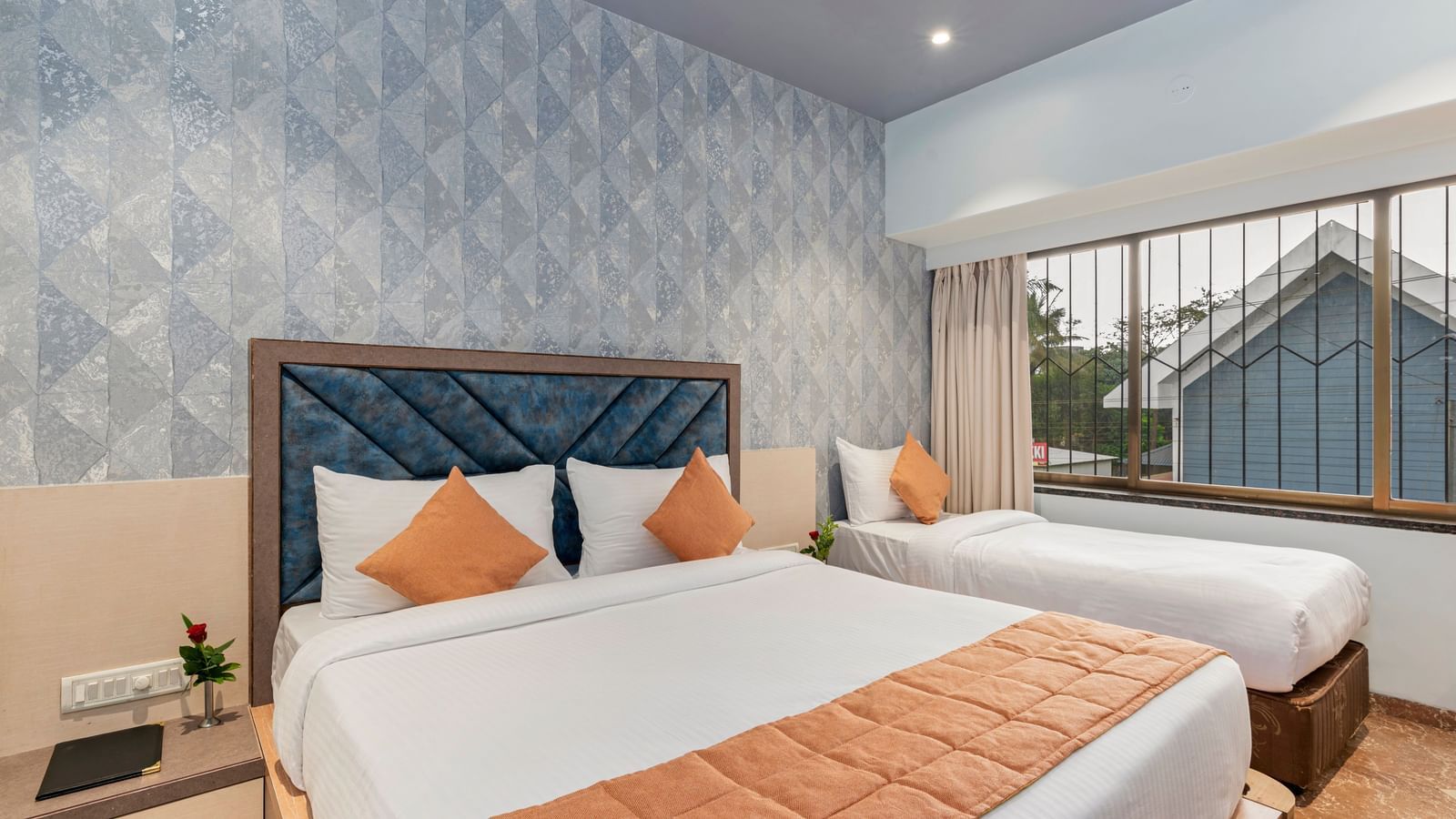 Double bed and a single bed setup at Emerald Retreat, Tungarli with a soft blue accent wall, large windows, and ample natural light.