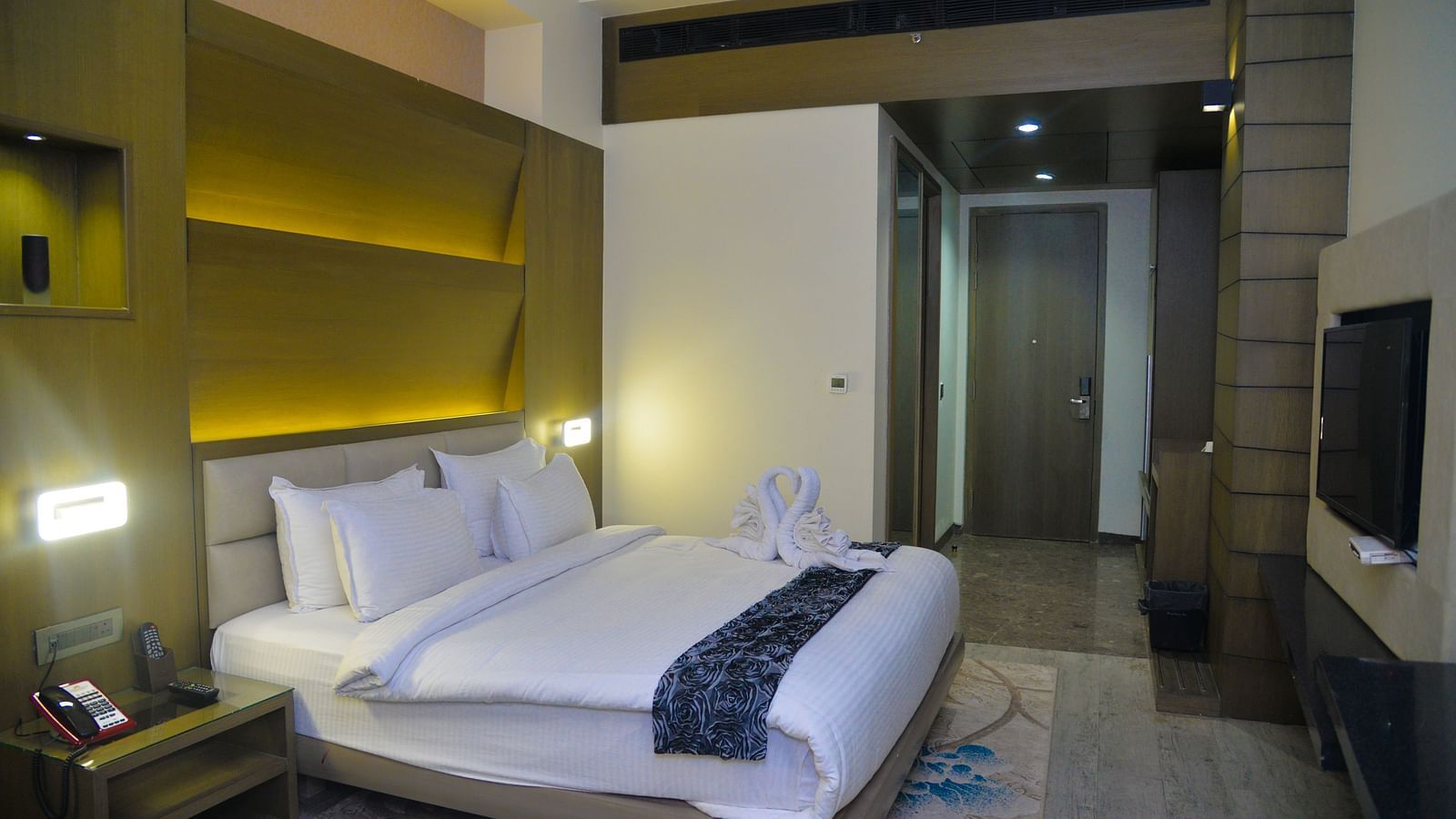 a room featuring a well decorated bed a side drawer a TV and a wardrobe - Golden Blossom Imperial Resorts Lucknow