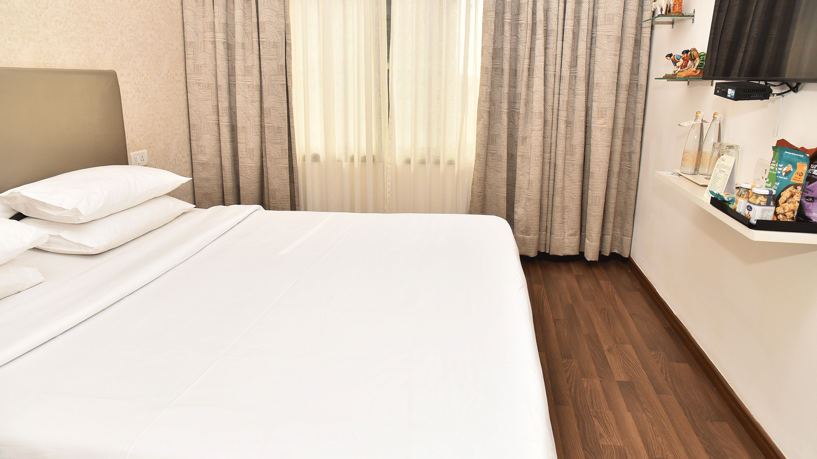 An image of a bedroom in our suite in Kanchipuram, with a large bed positioned in front of a wall-mounted television - Regency Kanchipuram by GRT Hotels