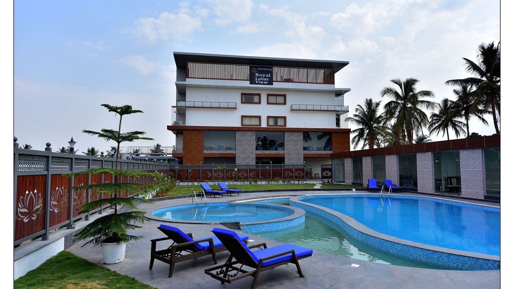 a grand swimming pool in front of resort facade with sunbeds in front and blue sky as the backdrop - Royal Lotus View Resotel