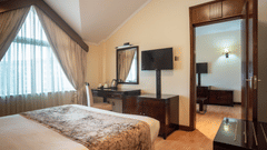 Suite at Boma Inn Nairobi a bed facing a TV on the wall mounted next to the doorway and a mirror on the other side of it near the window