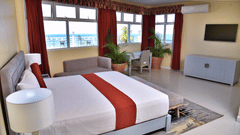 Deluxe Ocean View Room featuring a double bed facing the TV mounted on the wall with 3 sets of windows next to it at Hotel Grand A View in Montego Bay