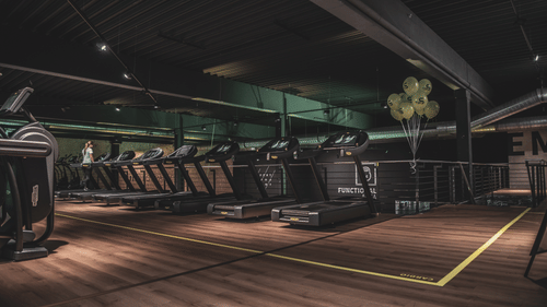 A dimly lit gym with treadmills stacked in a line