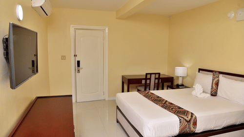 Standard Room at Hotel Grand A View featuring a plush bed facing the TV mounted on the wall over a running table and a work desk with a chair placed by the door