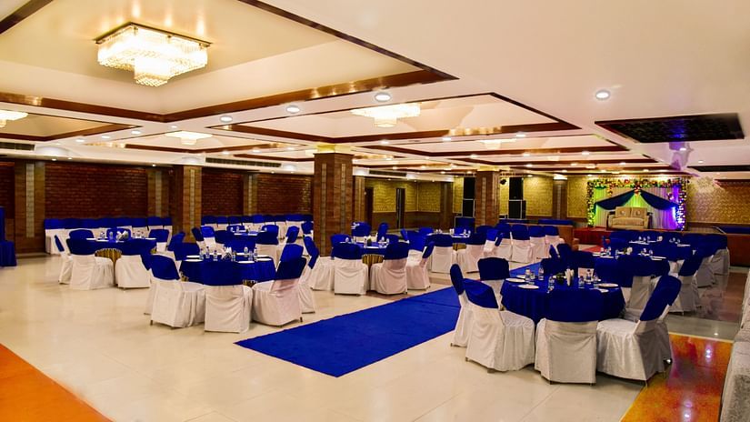 A banquet space with modern decor, bright lighting and white and blue chairs and a blue carpet laid out. - Clarks Inn Express, Near Jammu Bari Brahmana Railway Station