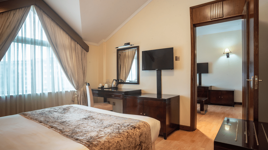 Suite at Boma Inn Nairobi a bed facing a TV on the wall mounted next to the doorway and a mirror on the other side of it near the window