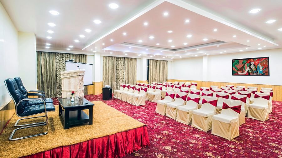 A spacious hall with neatly arranged chairs and a podium featuring a table and chair at Hotel Singge Palace.