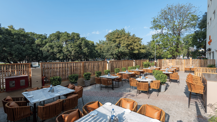 Open-air dining area at Mango Grove featuring wooden tables, comfortable seating, and lush surroundings.