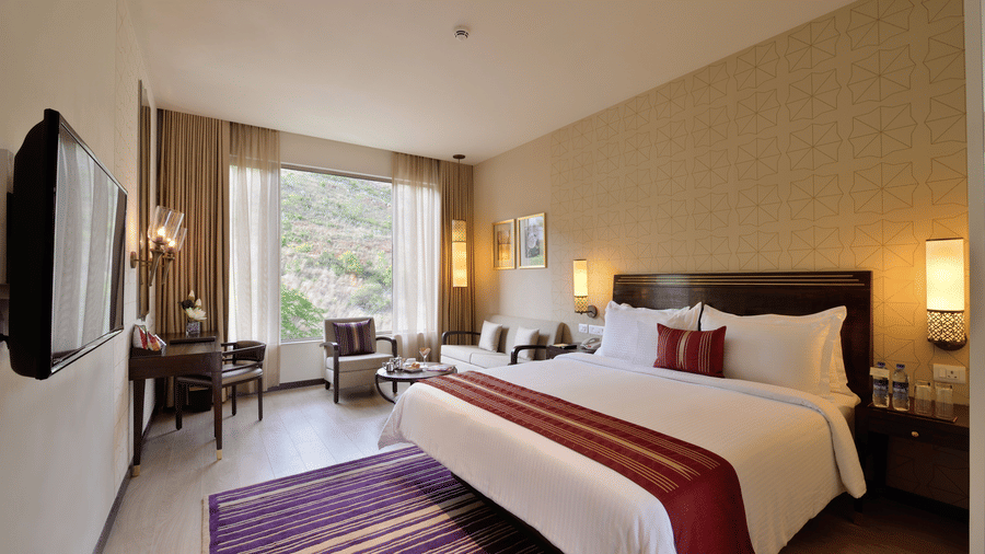 Deluxe Room at Marasa Sarovar Premiere, Tirupati with a king size bed, elegant furnishings, cosy seating corner, and large windows overlooking the surrounding landscape.