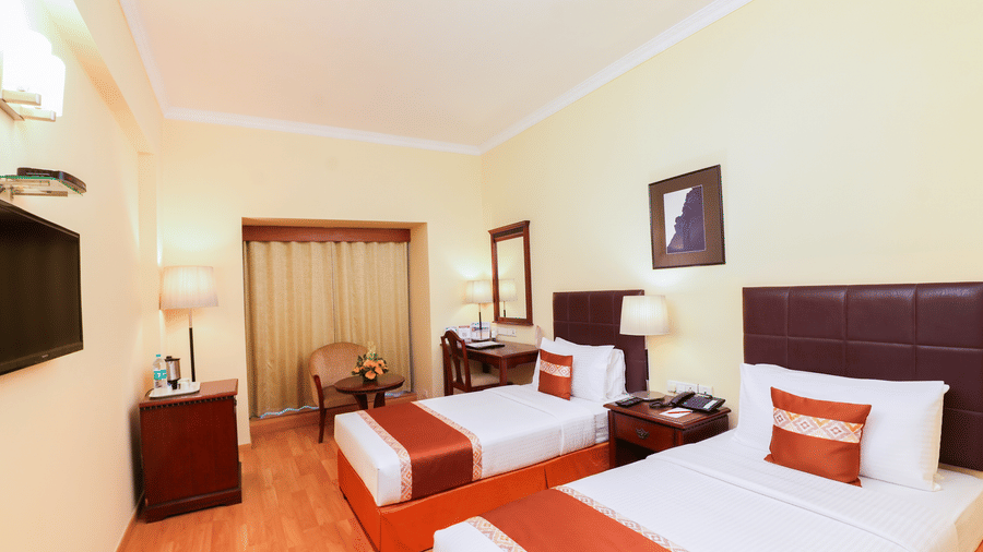 A room with twin beds, spreads, pillows, chairs, a table, wall arta, and a window with curtains. | MGM Mark Whitefield