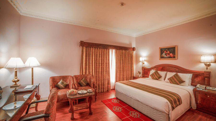 A warmly lit Superior Room offering the best accommodation in Chennai, with a king size bed, wooden decor, and cosy seating area by the window at Raj Park Hotel - Chennai