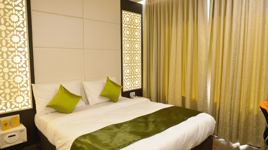 A bed with green runner and pillows beside curtained windows at The Onyx.