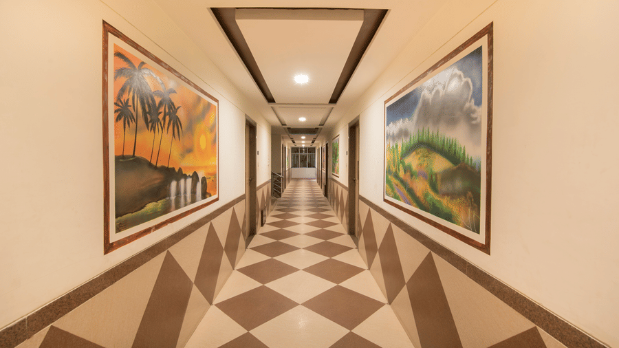 A long hotel hallway corridor featuring a diamond-checkered tile floor and framed nature paintings.