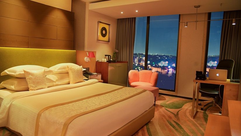 legant and spacious room at The Regnant Hotel featuring a plush bed, work desk setup, and ambient lighting with city views.