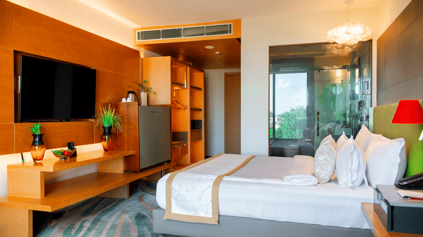 Bedroom at The Regnant hotel, Lucknow featuring a bed, a flat TV screen, wardrobe, minibar, tea and coffee maker, and a attached bathroom.