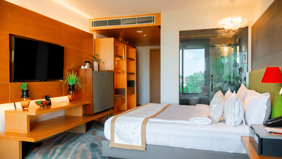 Bedroom at The Regnant hotel, Lucknow featuring a bed, a flat TV screen, wardrobe, minibar, tea and coffee maker, and a attached bathroom.