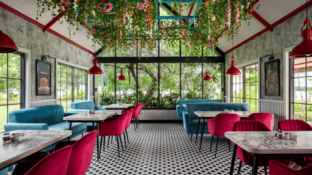 Wide view of a restaurant with glass walls, showing chairs, booth seating, and floor tiles under extensive ceiling decorations at Hotel Sonar Bangla, Taki.