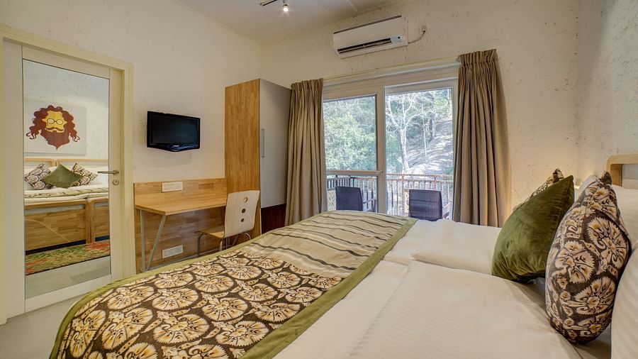 A bedroom with windows opening into the balcony offering forest views and a large bed facing a television - Bedzzz, Rishikesh