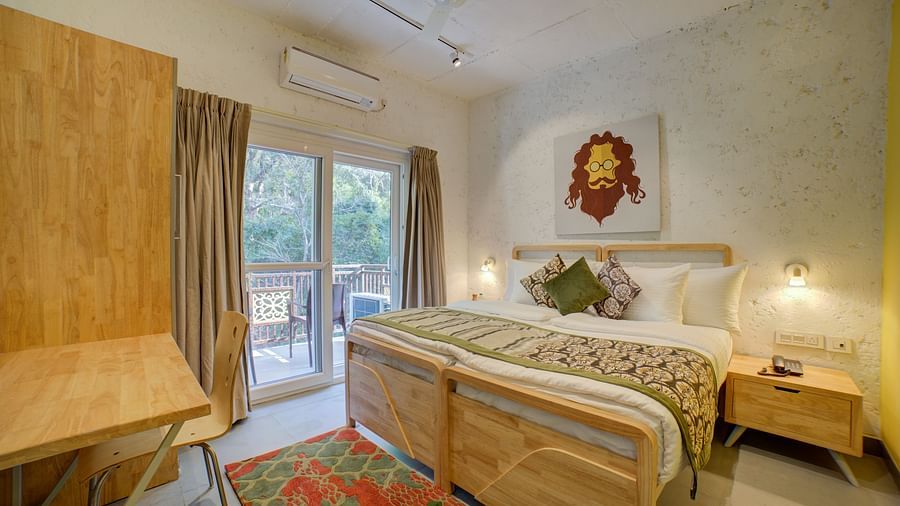 A bedroom with a large bed beside large windows opening into a  balcony with forest views outside - Bedzzz, Rishikesh