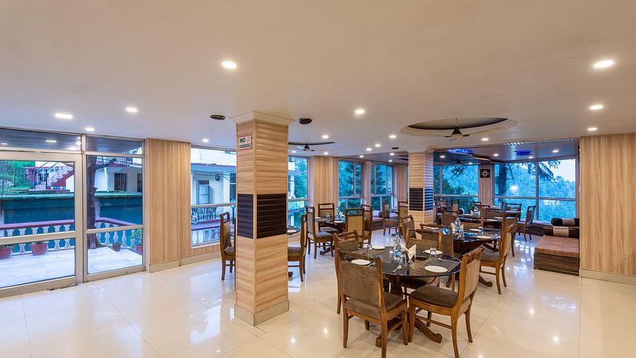 A wide angle shot of a dining area inside the resort featuring tables and chairs | DLS Anupam Resort, Dharamshala