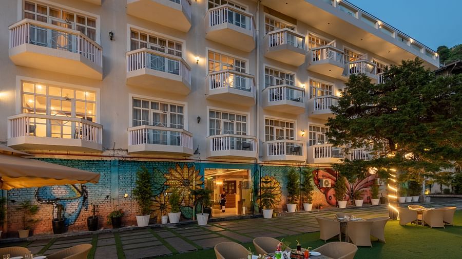 Facade view of DLS Highland Resort and Spa, Mussoorie with comfortable chairs in the lawn at dusk.