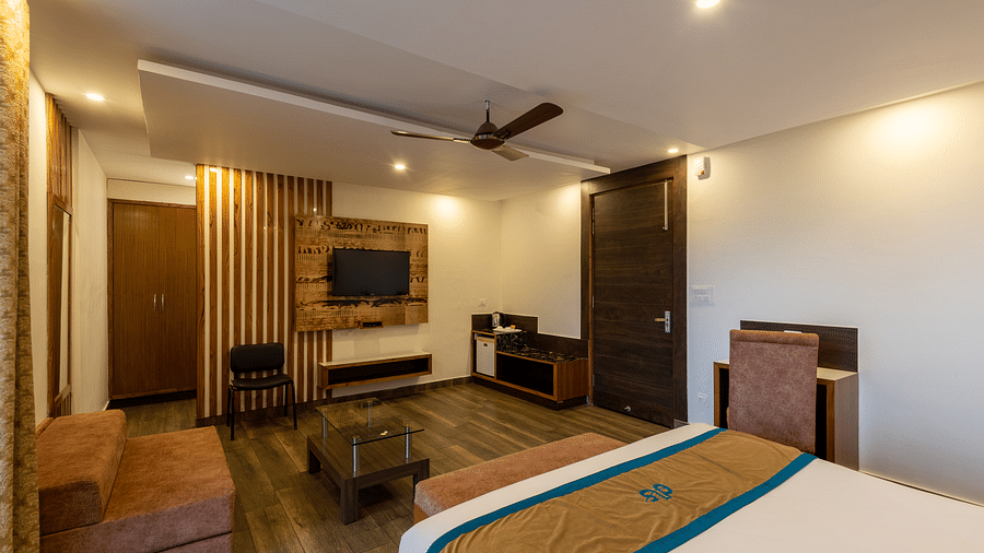 Premium room with modern wooden decor, TV, mini fridge, and a seating area - DLS Meghavan Resort, Dharamshala