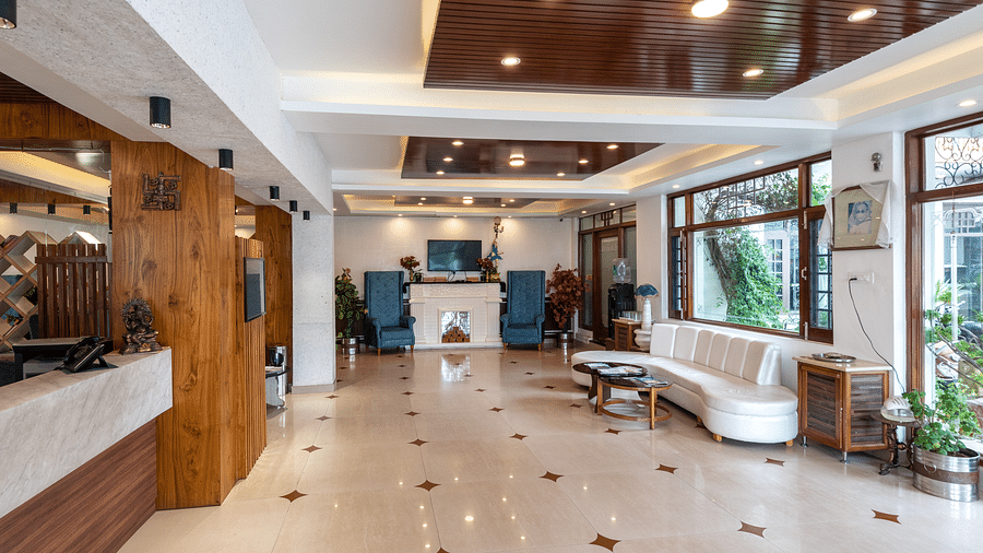 A hotel reception area featuring a white seating arrangement, blue armchairs, and a reception desk with wooden accents - DLS Meghavan Resort, Dharamshala