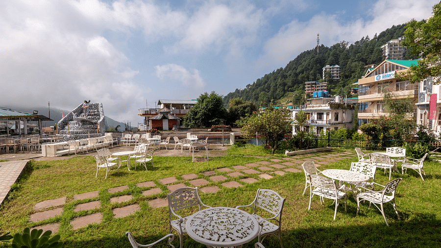 Outdoor seating area with tables and chairs on a lawn overlooking a mountain view - DLS Meghavan Resort