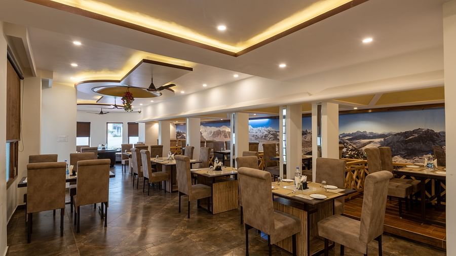 A spacious restaurant in Bhagsu with a modern design, featuring large mountain murals on the walls and rows of tables and chairs – DLS Meghavan Resort.