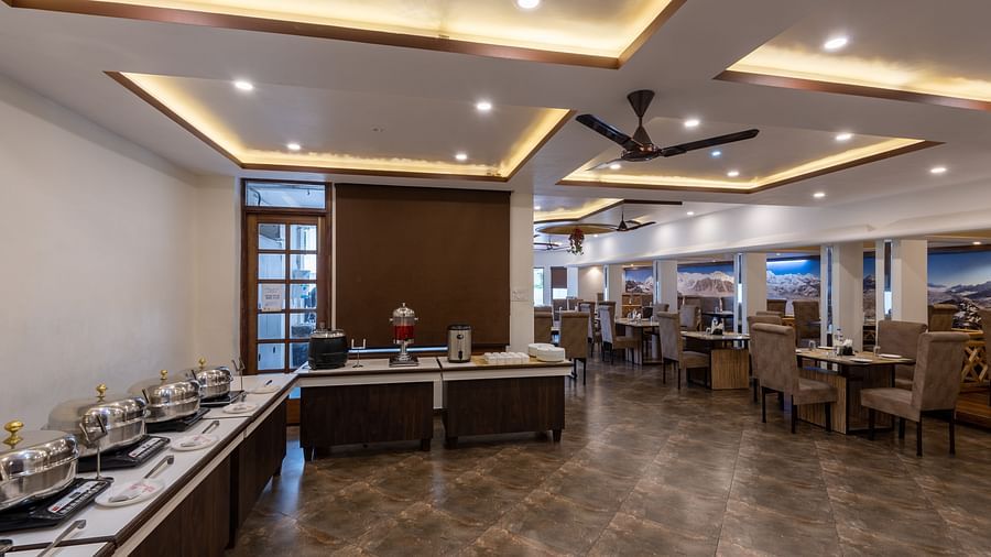 A dining room with tables and chairs, a buffet line, and a ceiling fan - DLS Meghavan Resort