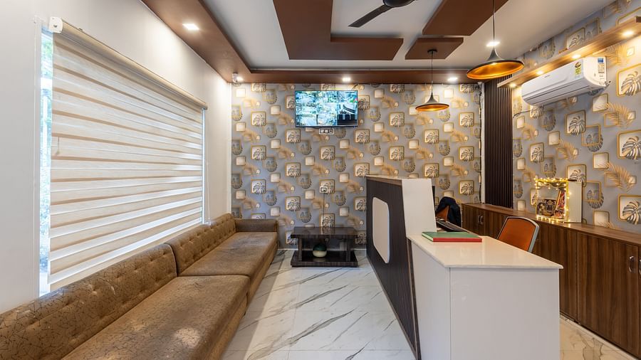  A modern reception area featuring a long cushioned bench, a white front desk with wood accents, patterned wallpaper, a ceiling fan, a wall-mounted TV, and ambient lighting - DLS Nature Trinket Resort, Dalhousie.