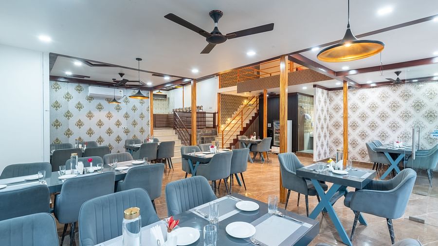 Stylish restaurant interior with neatly arranged tables, gray upholstered chairs, ceiling fans, and patterned accent walls - DLS Nature Trinket Resort, Dalhousie.