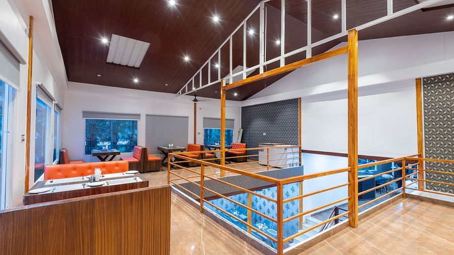 Spacious restaurant interior with orange booth seating, wooden railings, tiled floor, and large windows - DLS Nature Trinket Resort, Dalhousie.