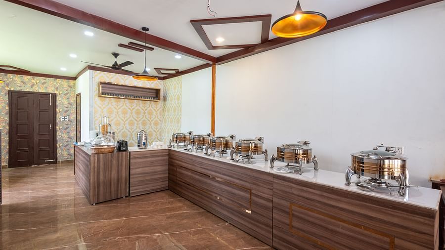 Buffet area in a restaurant featuring a long wooden counter with chafing dishes, warm lighting, and decorative wall accents - DLS Nature Trinket Resort, Dalhousie.