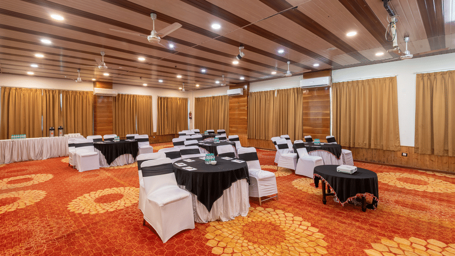 Bright banquet hall with orange carpet, tables and chairs.