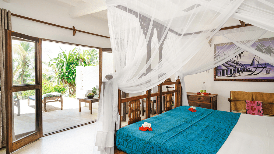 Bright bedroom with a wooden bed, mosquito net, glass doors, and a garden view - Shooting Star Boutique Hotel.