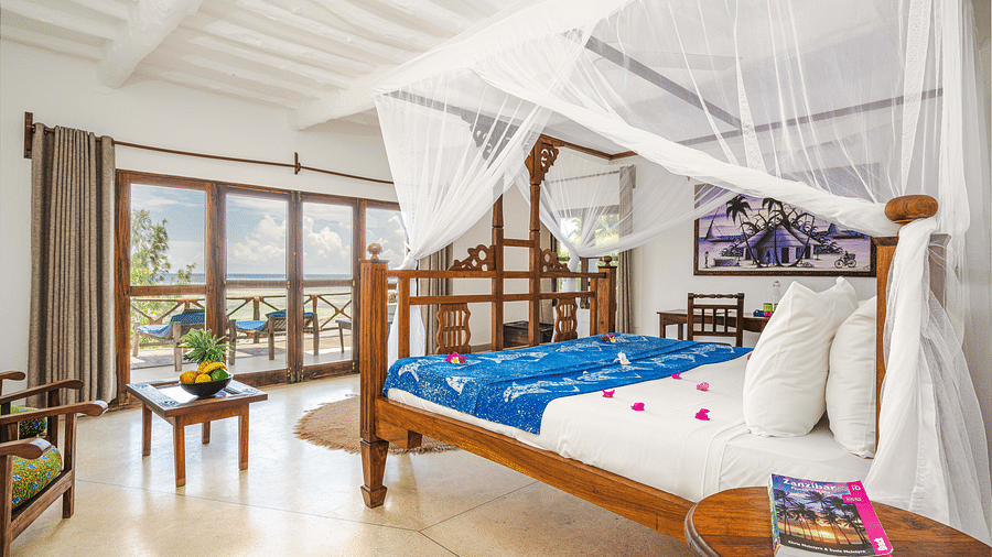 View of a room showcasing a large bed with mosquito nets and decorative pillows, a small table, and artistic wall hangings in Sea View Family Cottages - Shooting Star Boutique Hotel.