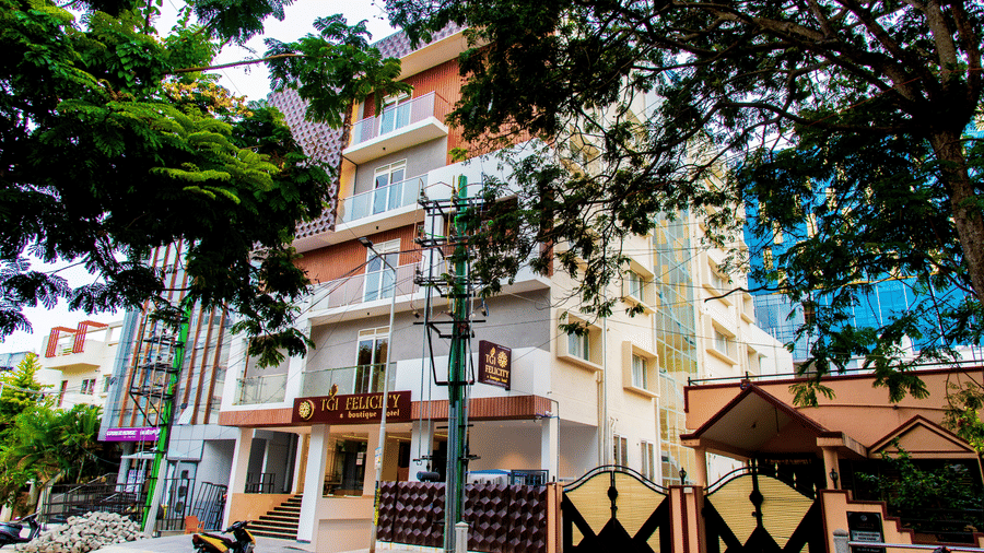 Multi-story building with balconies and gated entrance along tree-lined street in urban area - Felicity by TGI Hotel