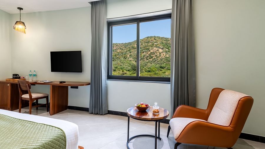 Valley View Room with a king size bed, seating area by the window, and a desk with a television at The Qualia Resort Club & Brewery, Udaipur.