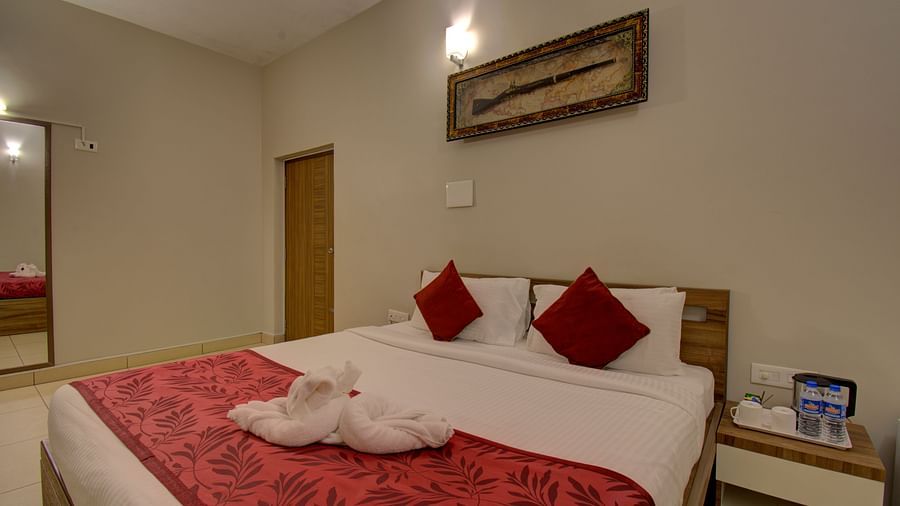 A swan made with of towel on a huge bed, a side table, mirror, wooden door and an wall art | Superior Room | Woodstock Resorts, Coorg