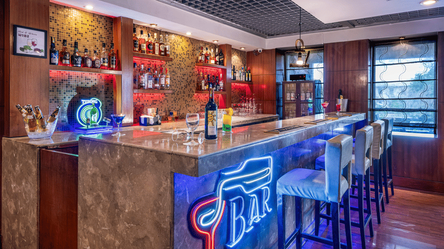 Distil Bar with neon lights, bar chairs, false ceiling, and wooden walls at Lords Plaza Jaipur.