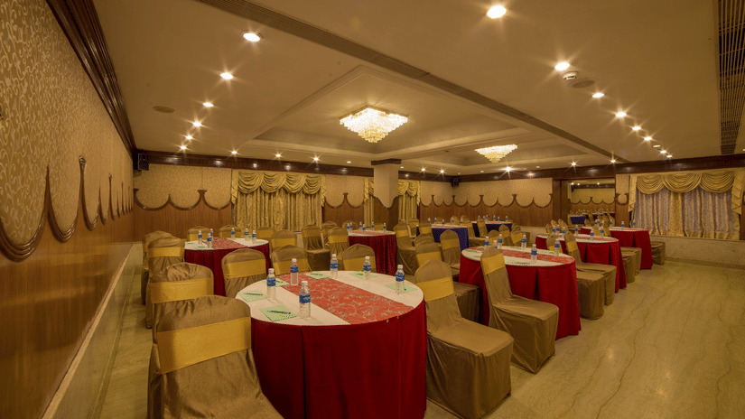 Seating area at Summit conference hall at Raj Park Hotel in Chennai , featuring  chairs, tables, and chandeliers.