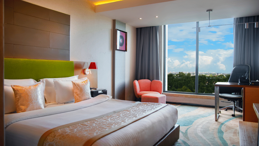 Bedroom at The Regnant featuring double size bed, a sofa,  a work desk and chair, and a large window with view.
