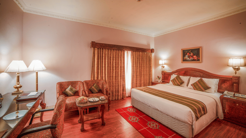 A warmly lit Superior Room offering the best accommodation in Chennai, with a king size bed, wooden decor, and cosy seating area by the window at Raj Park Hotel - Chennai