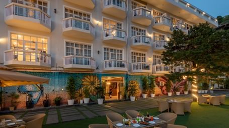 Facade view of DLS Highland Resort and Spa, Mussoorie with comfortable chairs in the lawn at dusk.